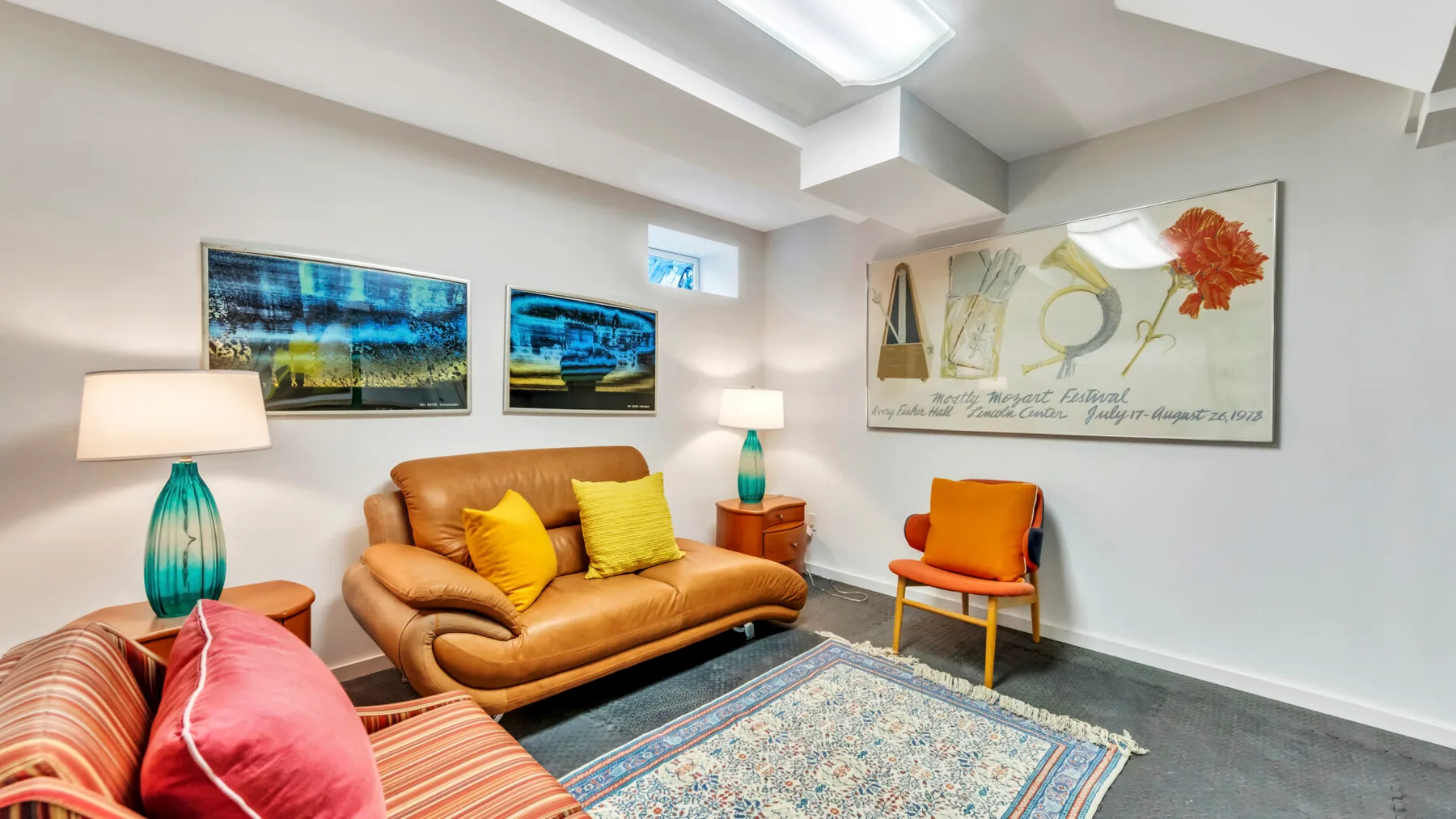A living room with a tan sofa, colorful cushions, and framed artwork.