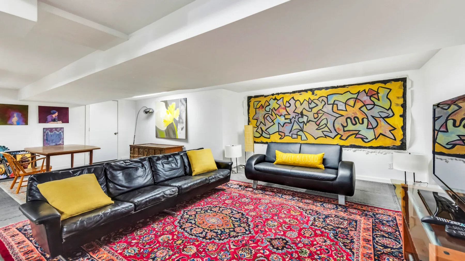 A living room with dark seating, colorful wall art, and a patterned rug.