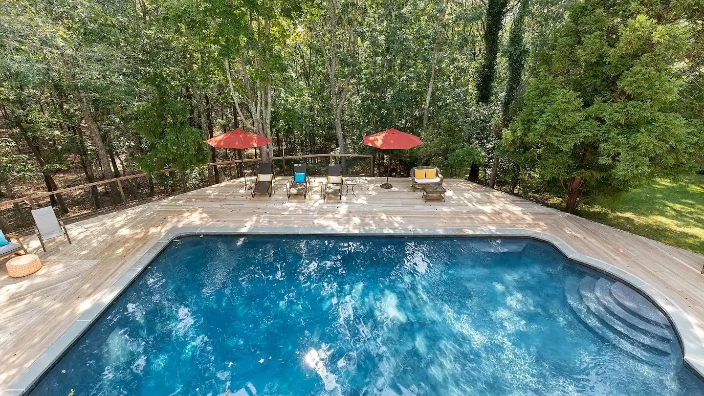 An outdoor swimming pool sits beside a paved deck surrounded by trees.