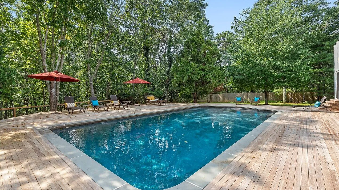 An outdoor swimming pool is surrounded by a wooden deck and leafy trees.