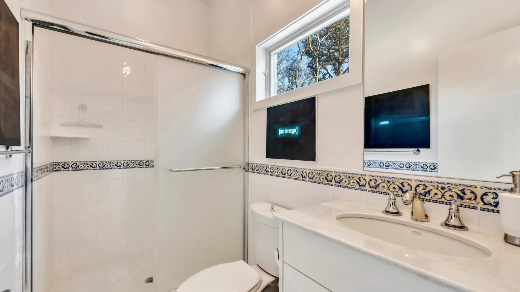A bright bathroom with a long vanity, sinks, and a glass shower.