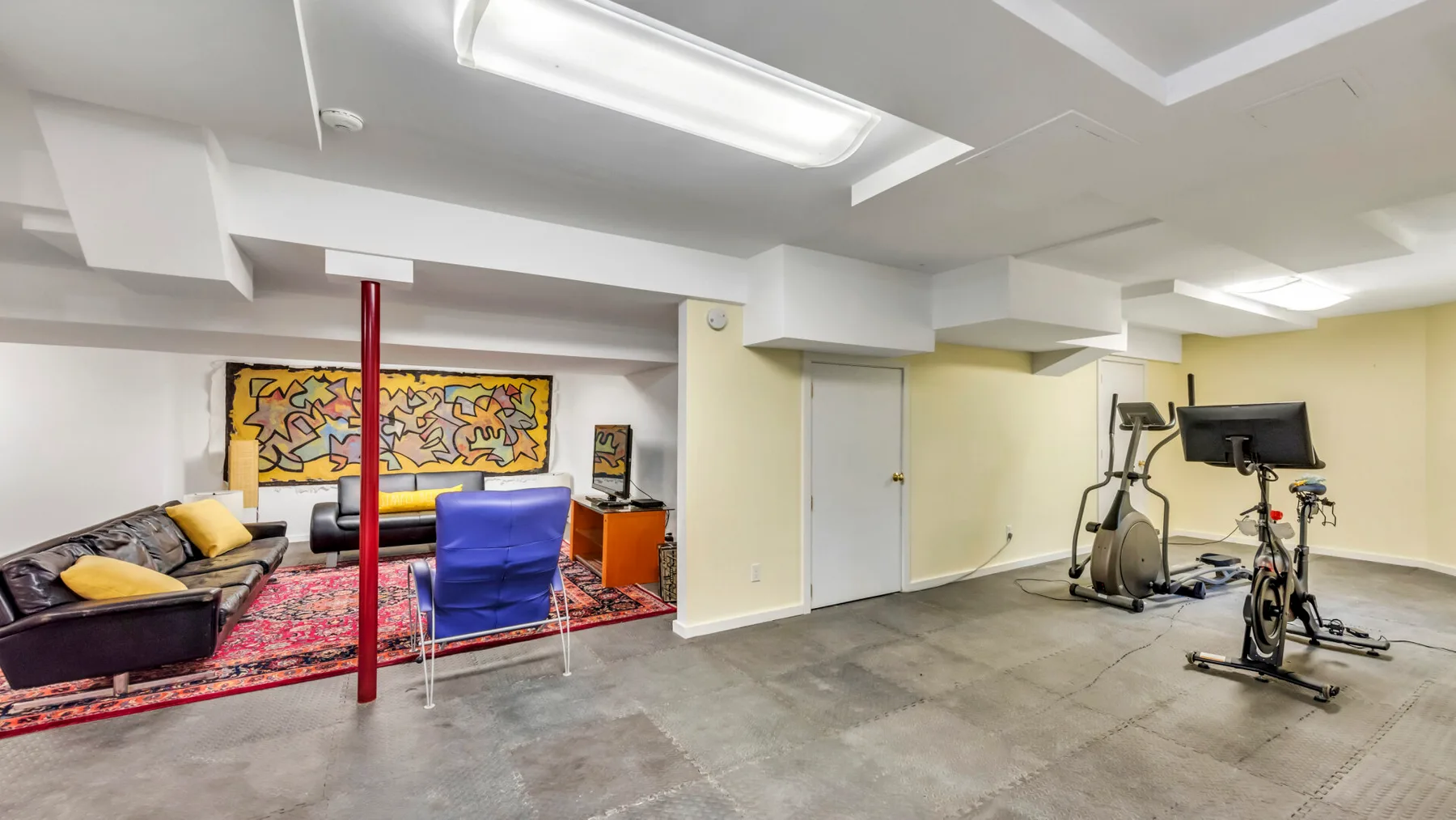 A basement recreation room with seating, colorful wall art, and exercise equipment.