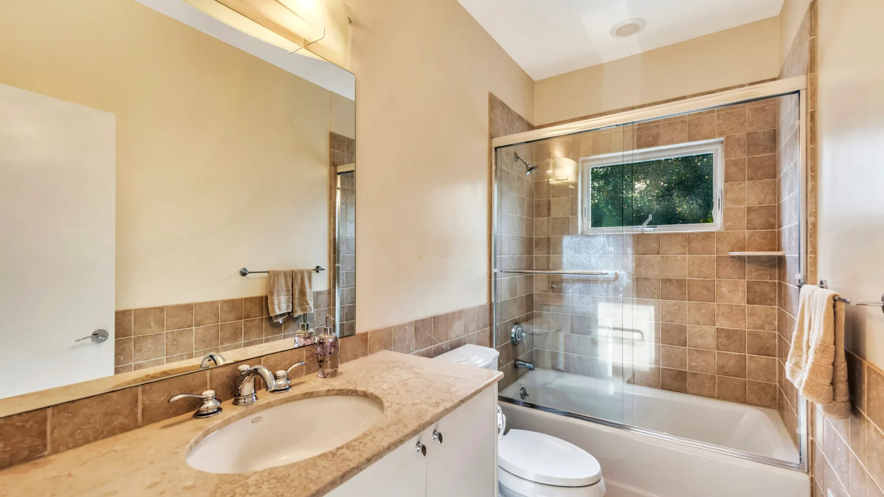 A bathroom with a long vanity and a bathtub beneath a window.
