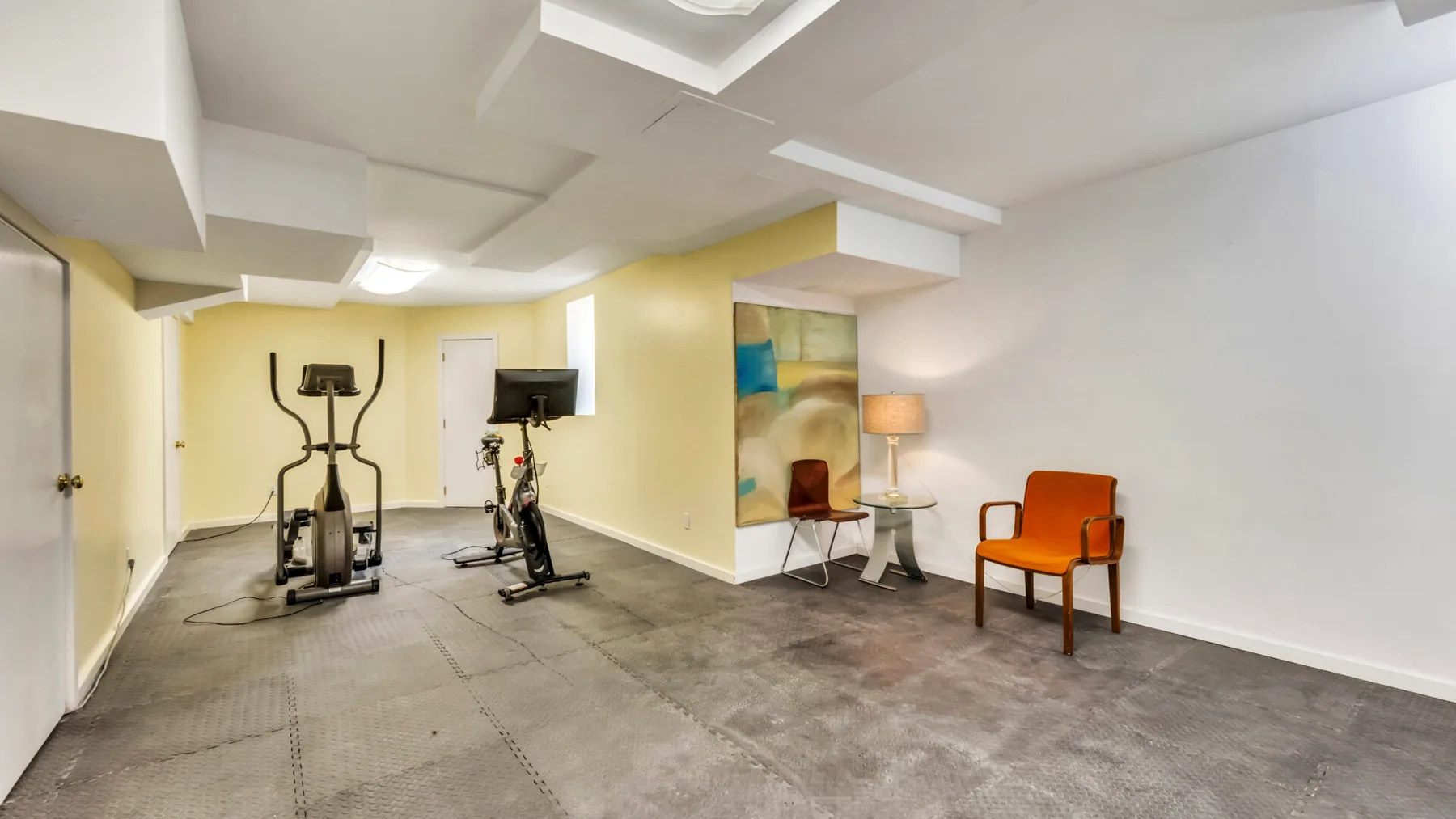 A basement exercise room with stationary bikes and seating along the wall.