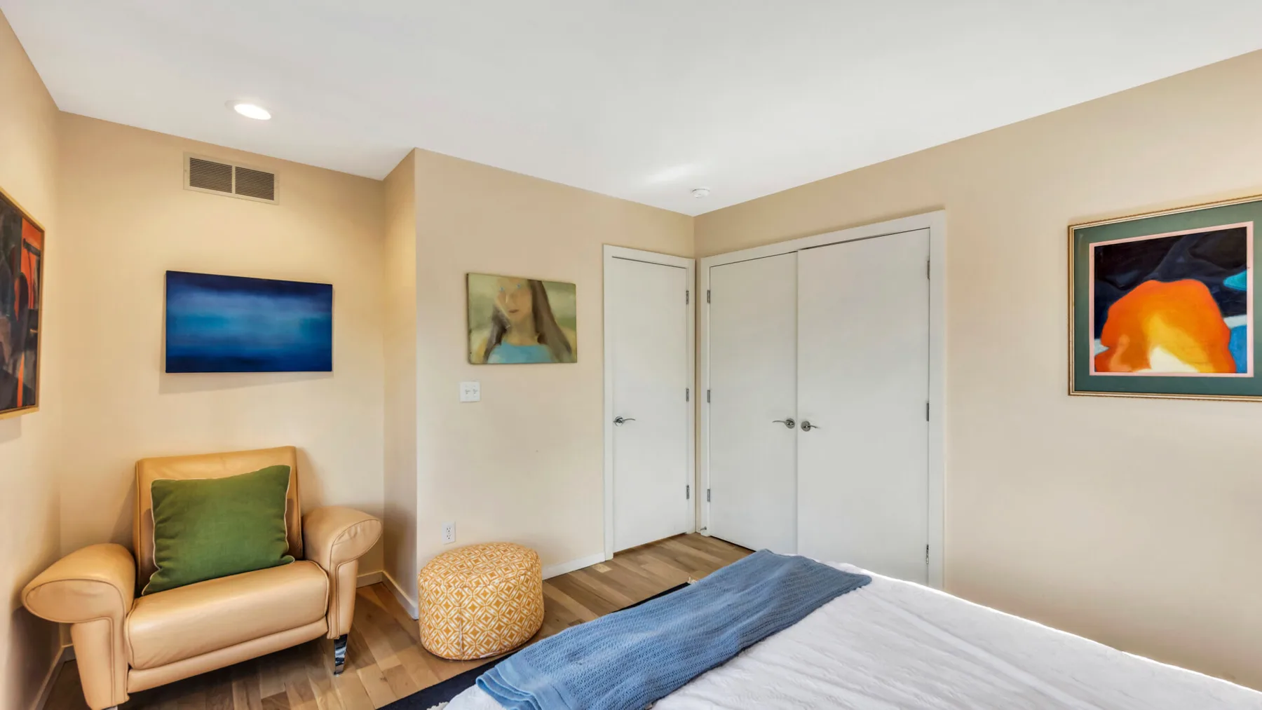 A bedroom with a bed, an armchair, and framed artwork on the walls.