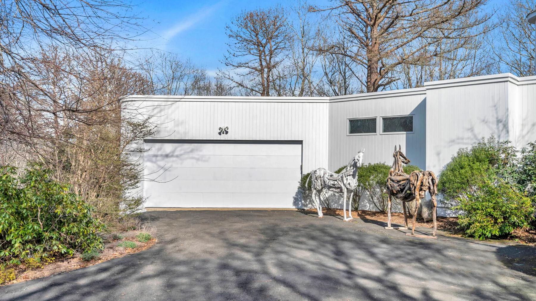 A modern white building with a wide garage door and two animal sculptures outside.