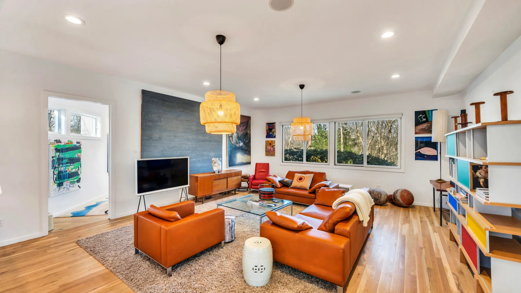 A bright living room with orange seating, a television, and large windows.