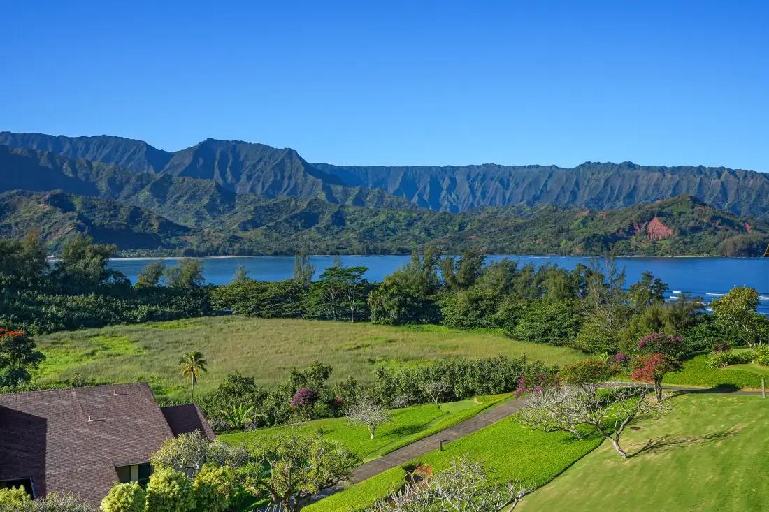 Un jardín verde y cuidado tiene vistas a un lago y una cordillera.