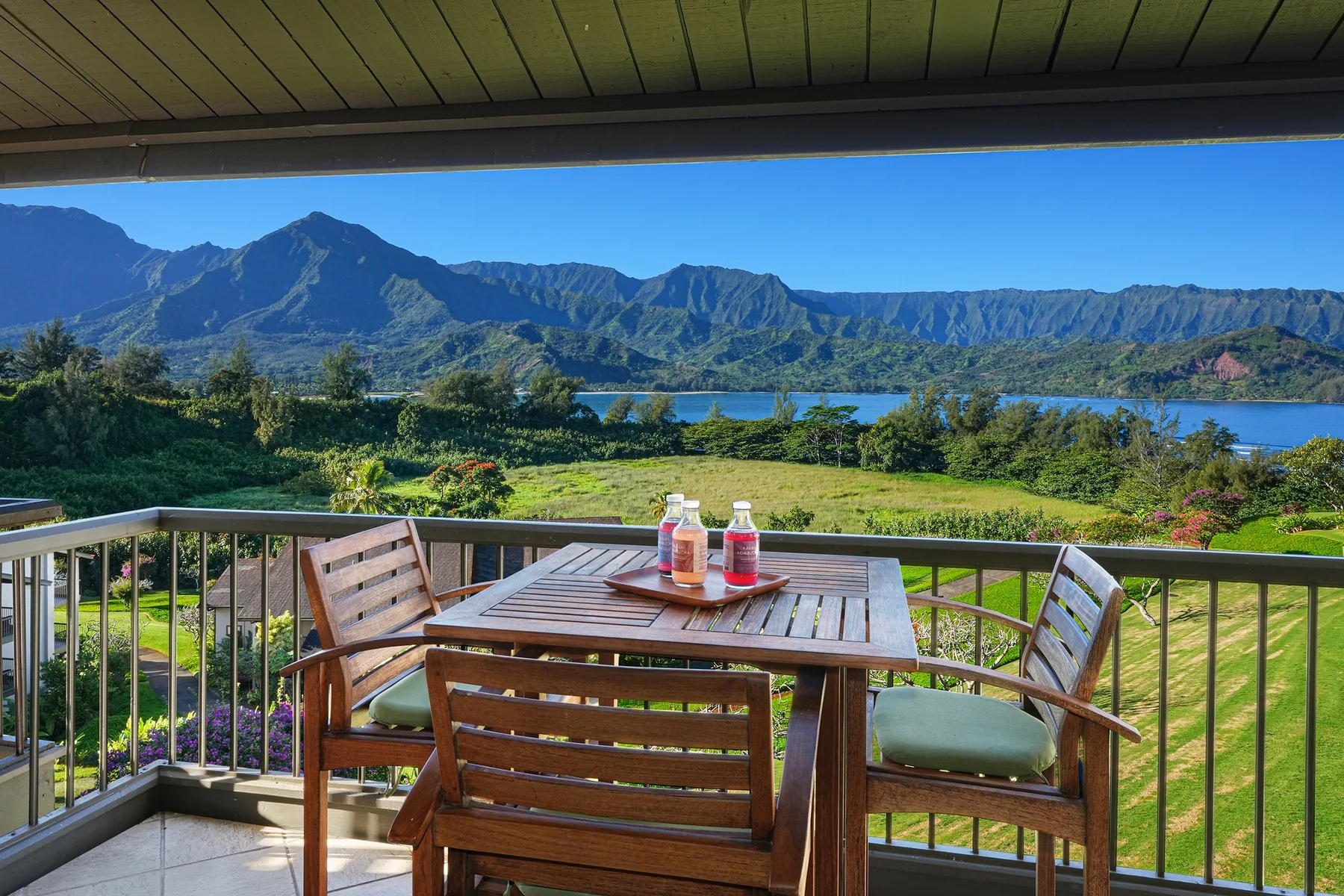 Una zona de estar en un balcón da a un paisaje verde, un lago y una cordillera.