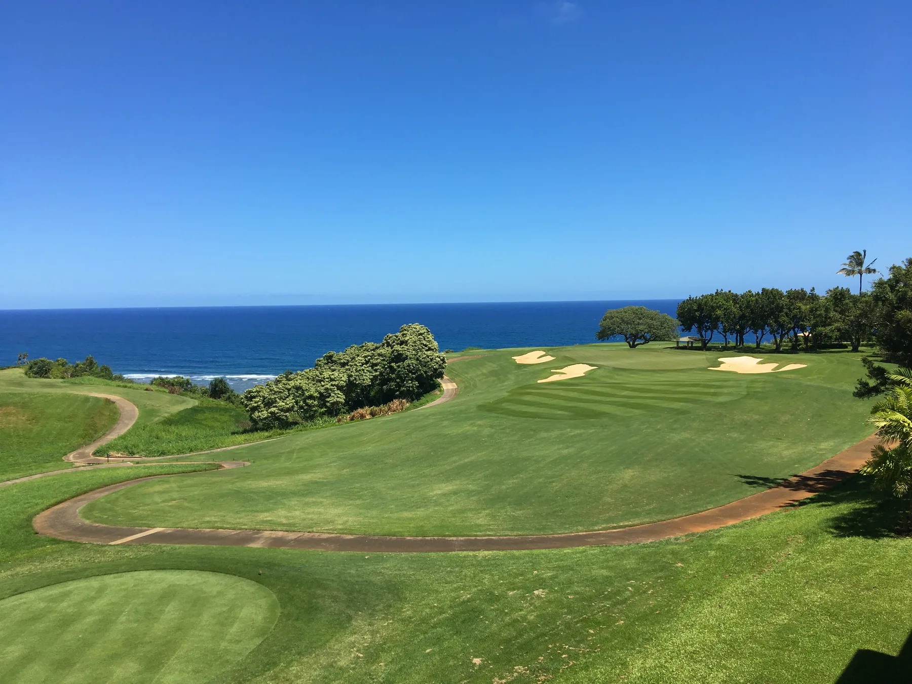 Un campo de golf cubierto de césped, con bunkers de arena, da al océano.