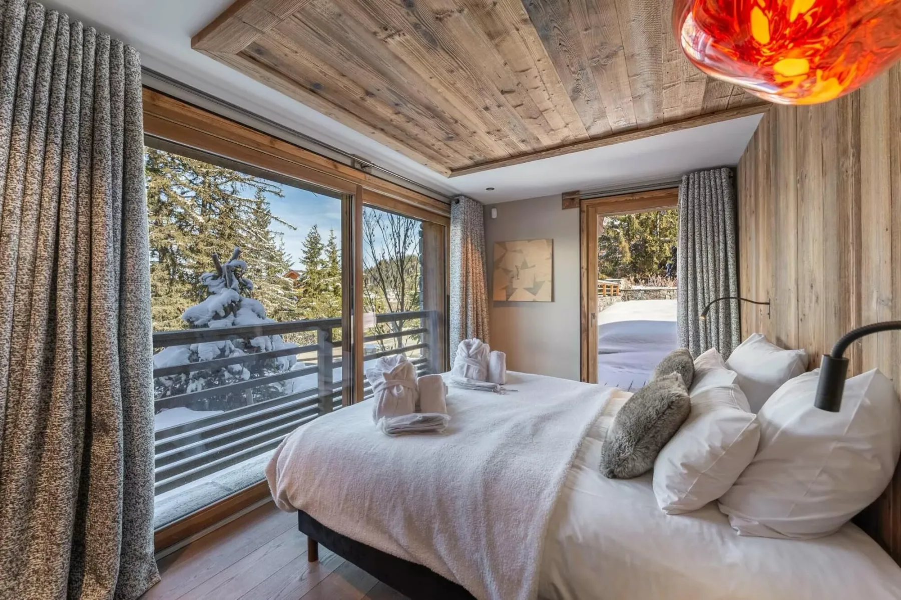 Un dormitorio con una cama junto a grandes ventanas que dan a un paisaje boscoso y nevado.