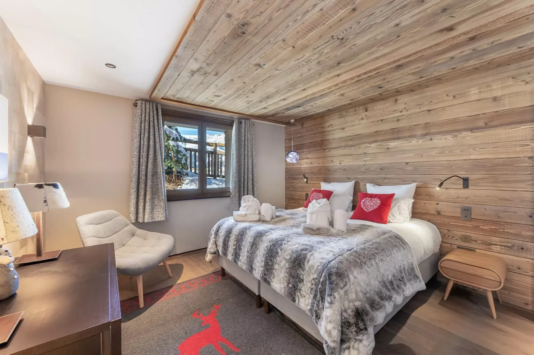 Un dormitorio con cama, sillón y ventana bajo un techo revestido de madera.