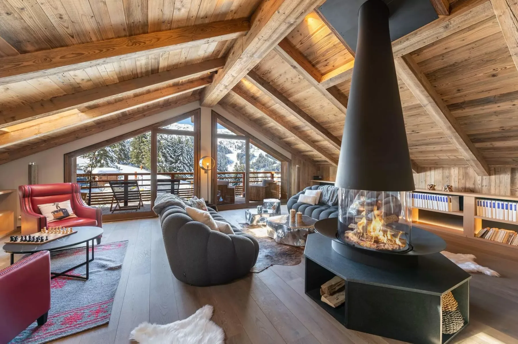 Una sala de estar amplia tiene asientos alrededor de una chimenea central bajo un techo de madera.