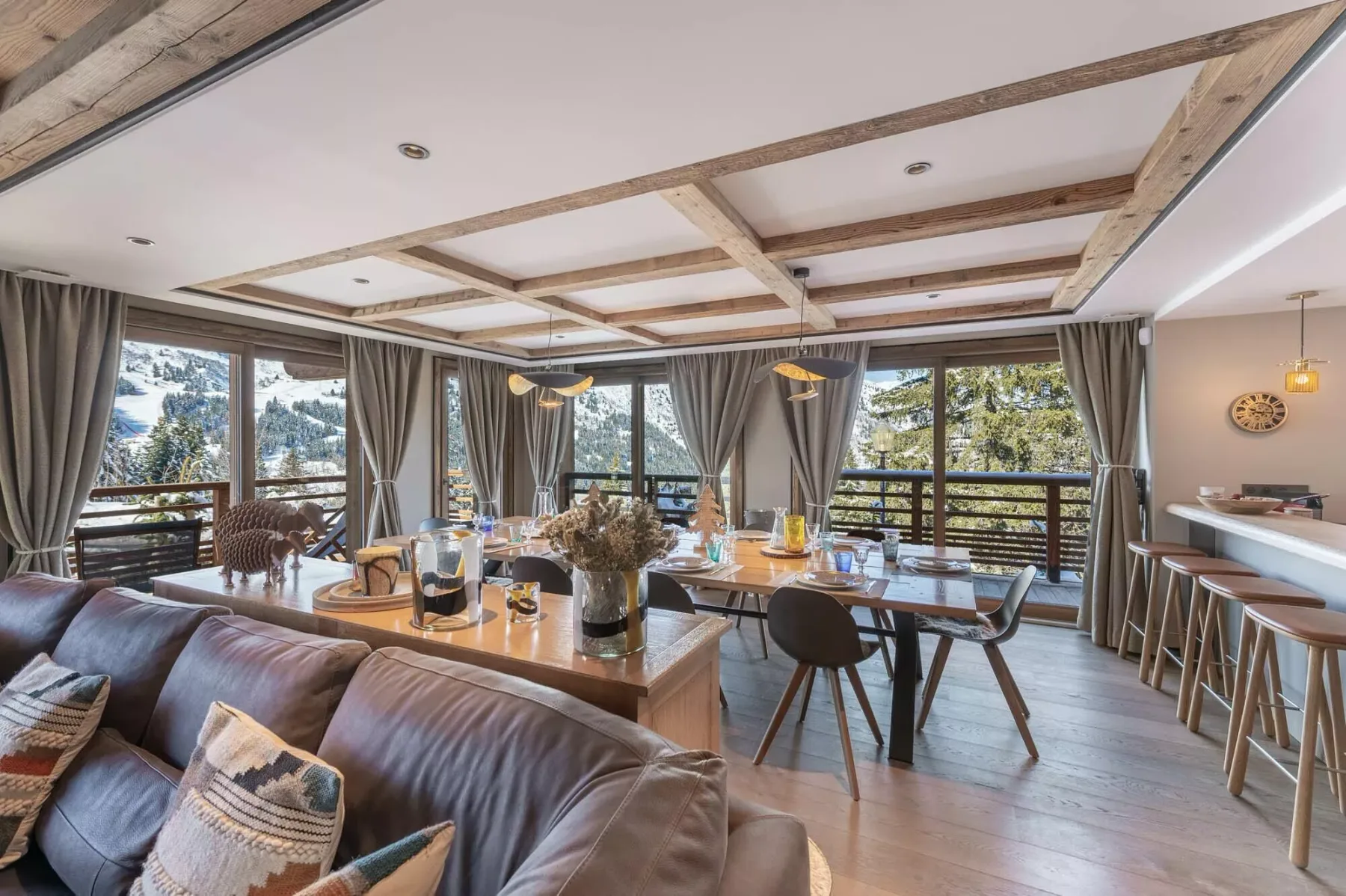Una zona de comedor y estar con una mesa larga, asientos y grandes ventanas con vista a los árboles.