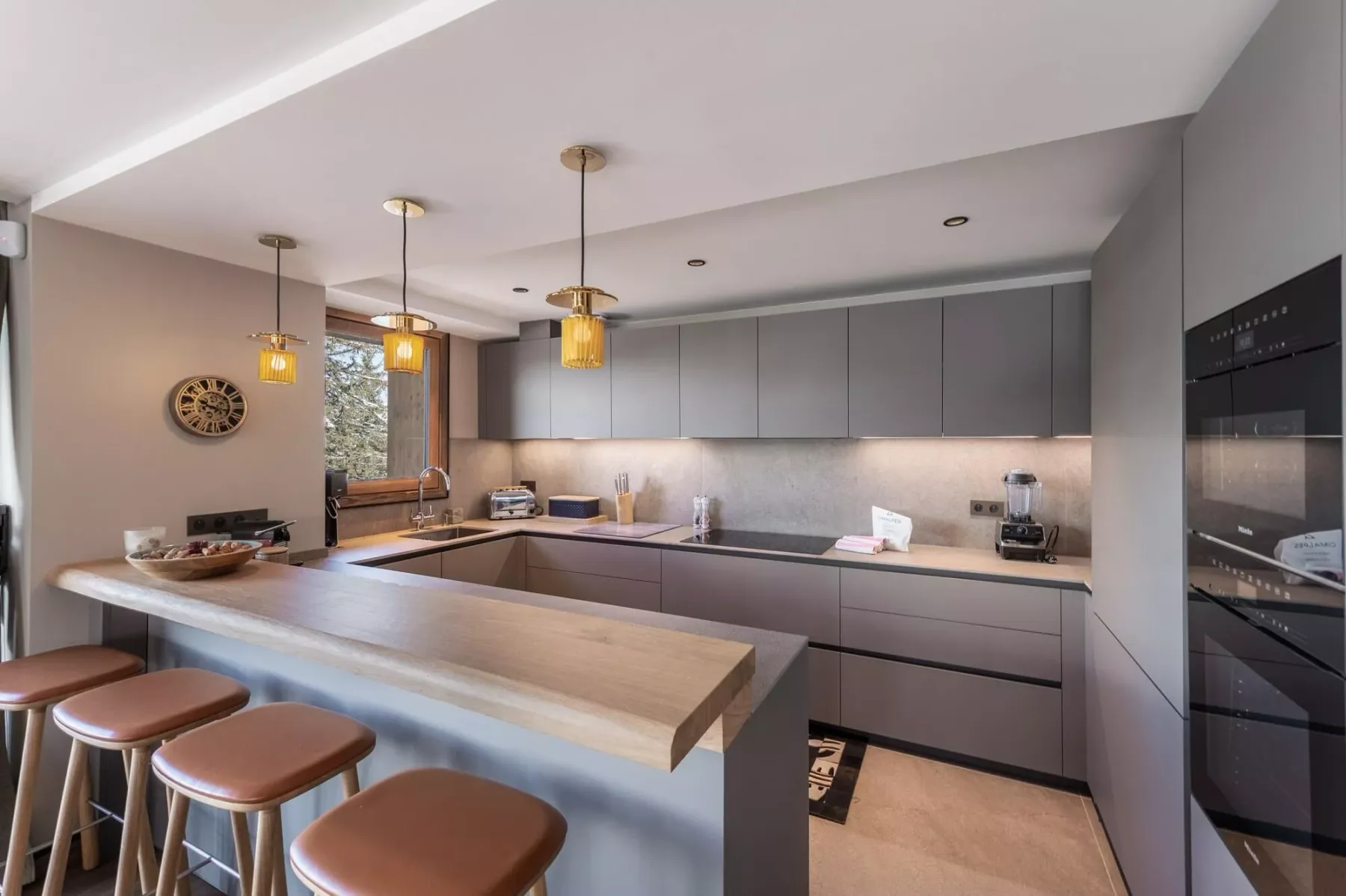 Una cocina moderna con gabinetes grises, una isla larga y luces colgantes.