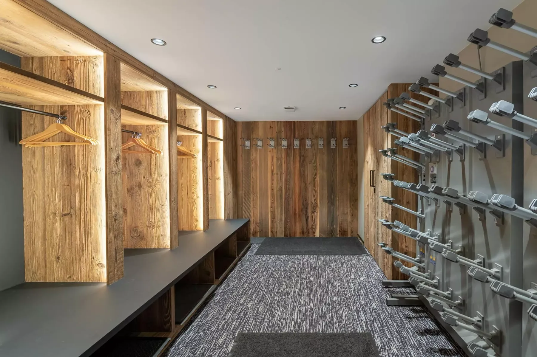 Un vestuario con taquillas de madera, un banco y filas de equipos de ejercicio.
