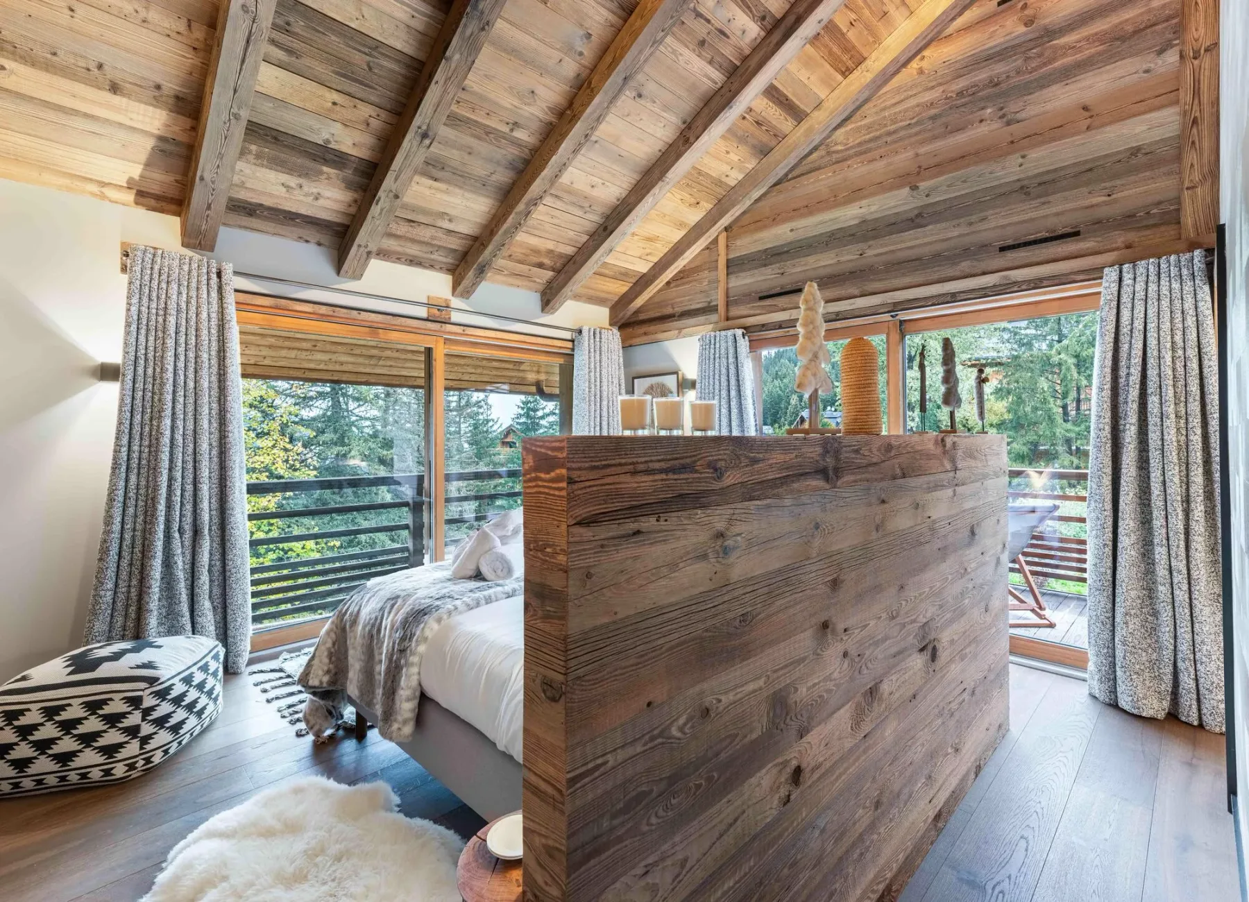 Dormitorio con un tabique de madera, vigas a la vista y grandes ventanas.