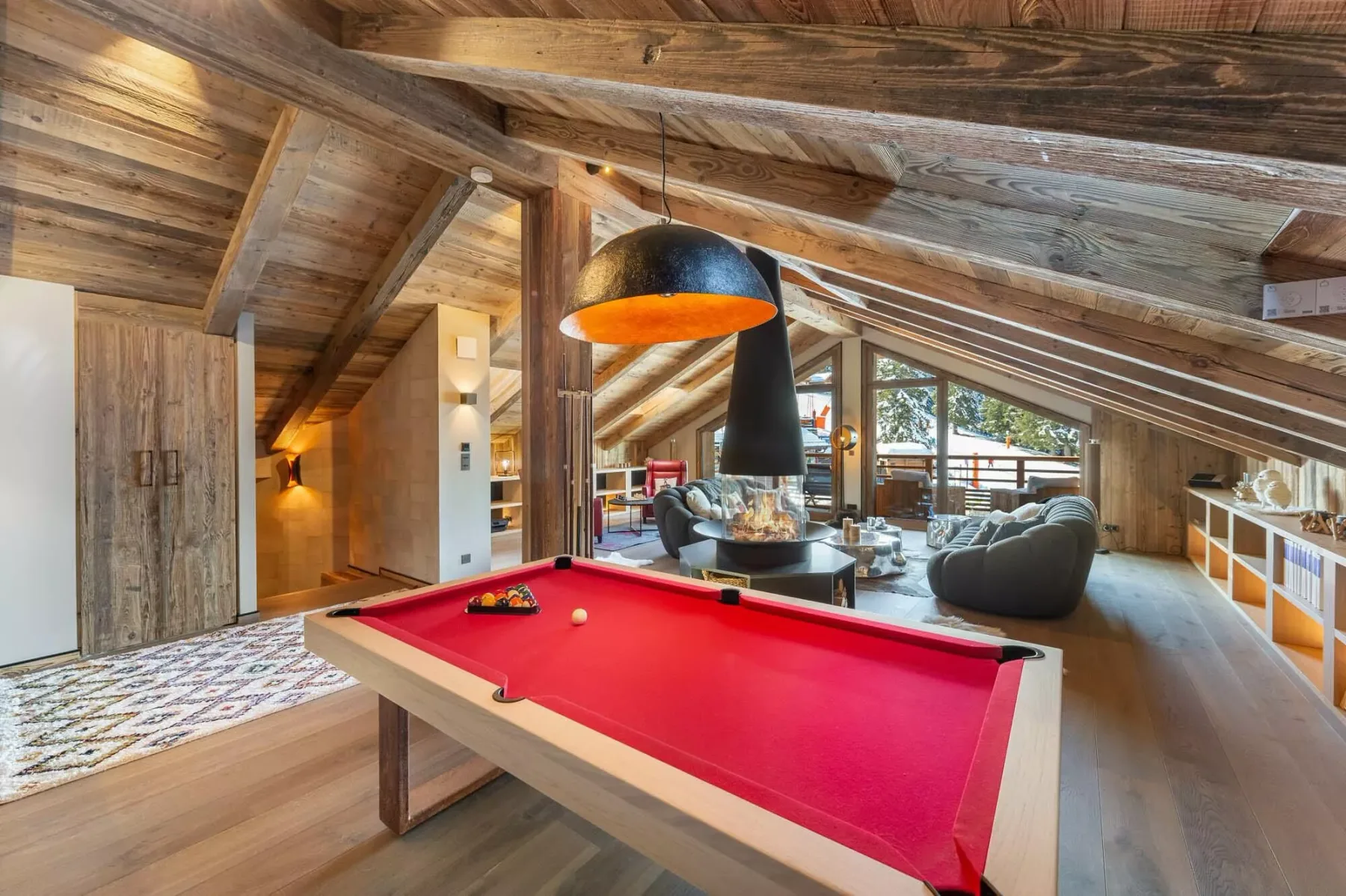 Una sala de juegos con una mesa de billar roja bajo un techo inclinado de madera.