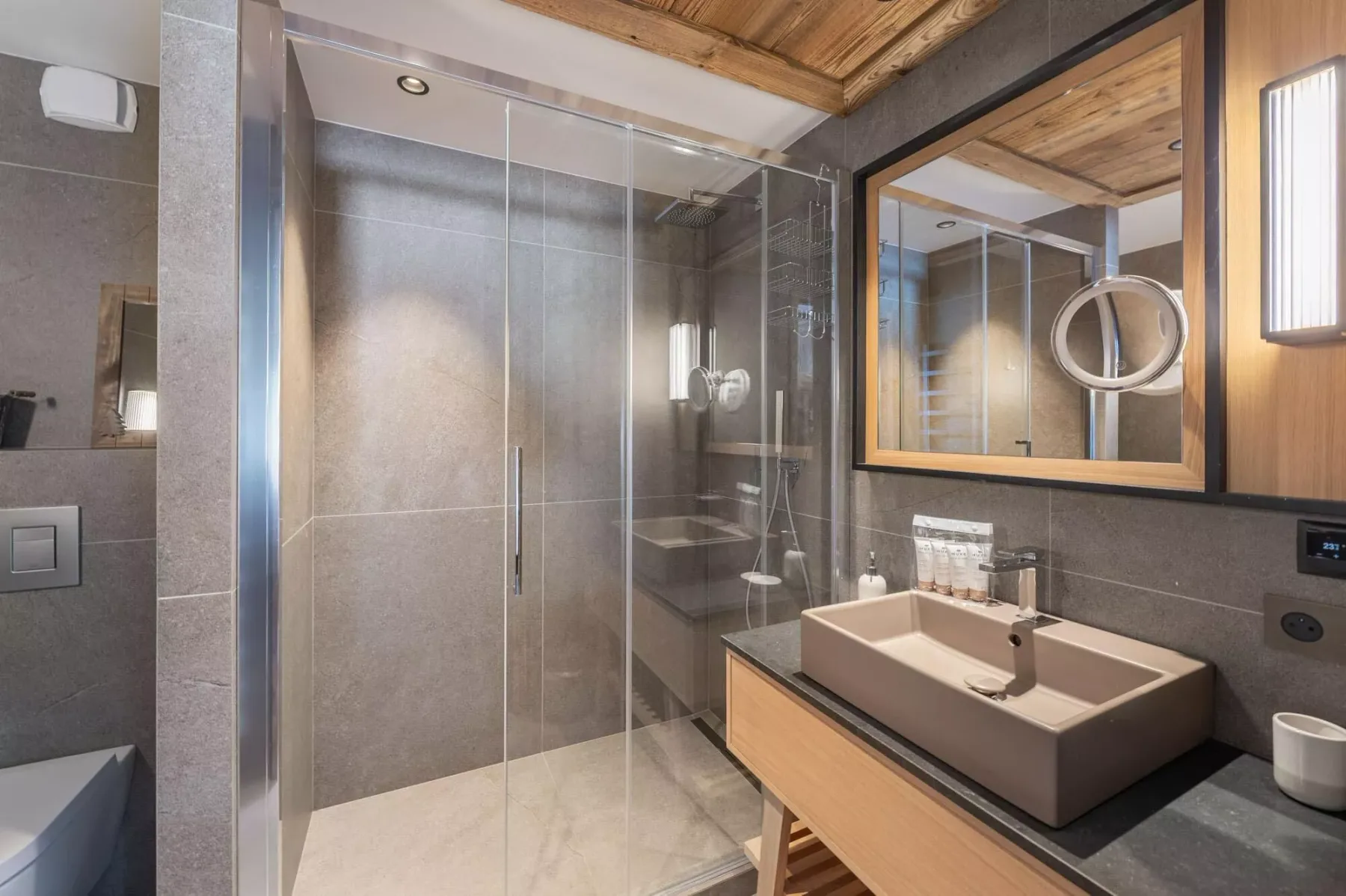 Un baño moderno con una ducha de vidrio y un lavabo amplio bajo un espejo.