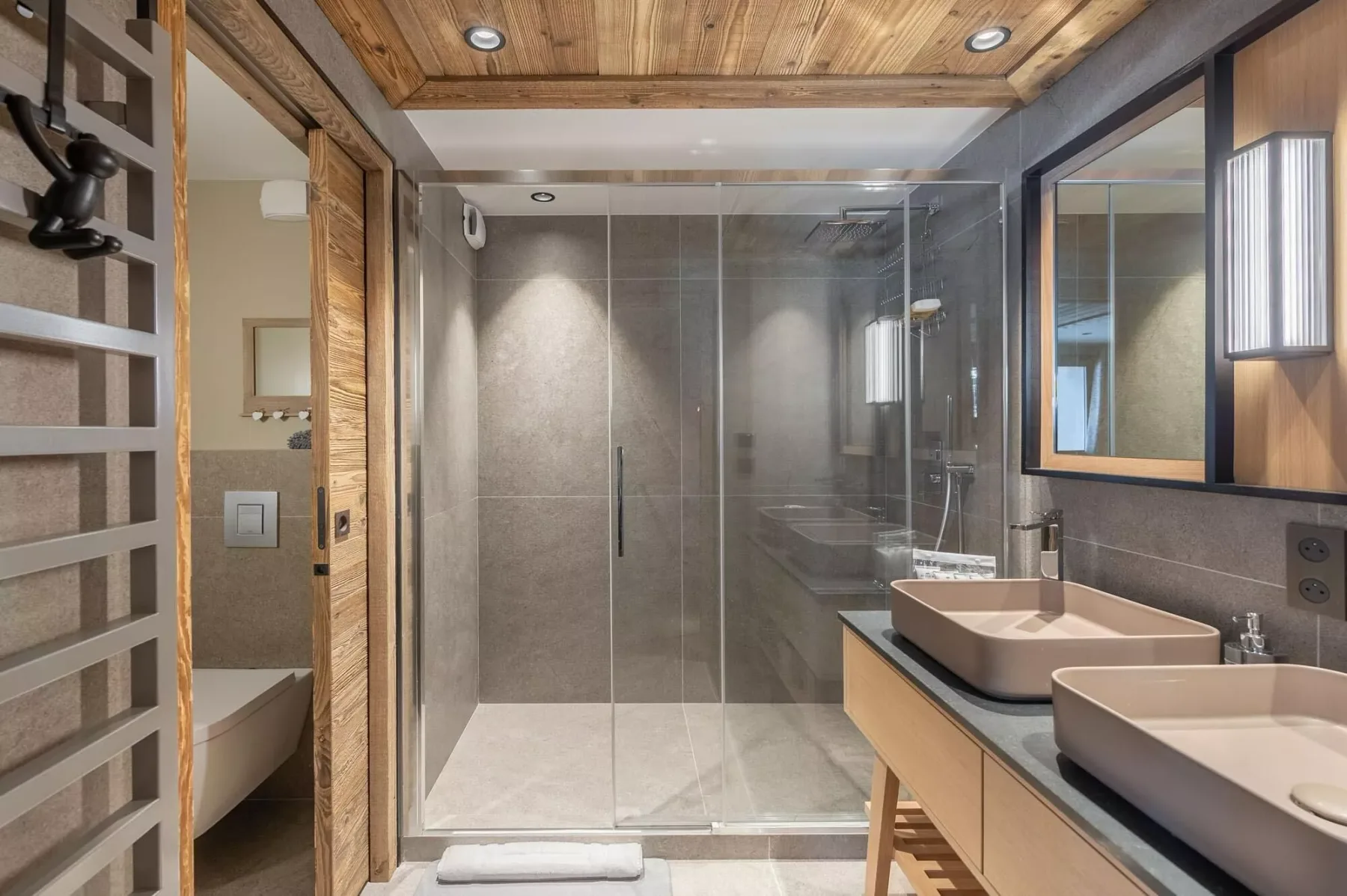 Un baño moderno cuenta con una ducha de vidrio y dos lavabos sobre encimera.