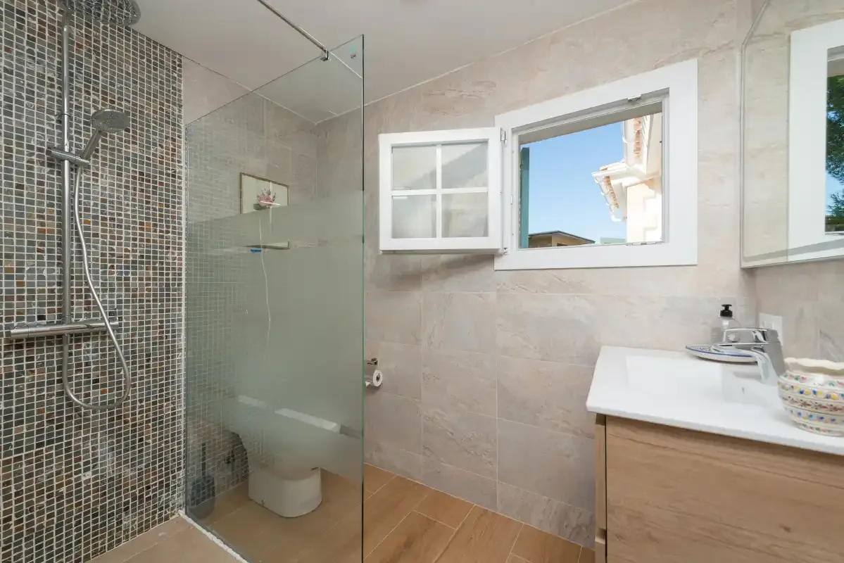Un baño con una ducha de vidrio y un tocador junto a una ventana.
