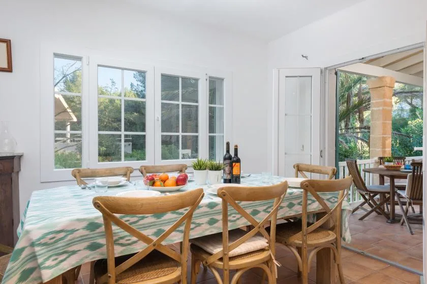 Un comedor luminoso con una mesa larga, asientos de madera y ventanales.