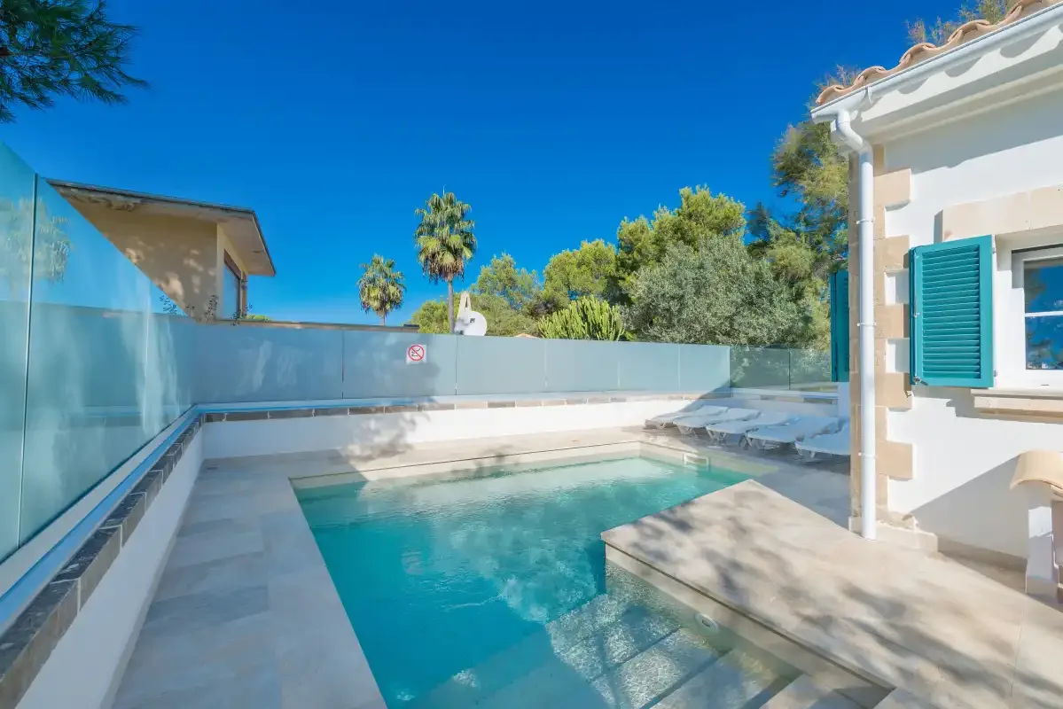 Piscina al aire libre junto a un edificio blanco, rodeada de paneles de vidrio y privacidad.