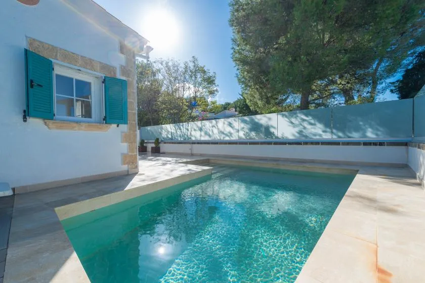 Una piscina está junto a un edificio blanco en un patio soleado al aire libre.