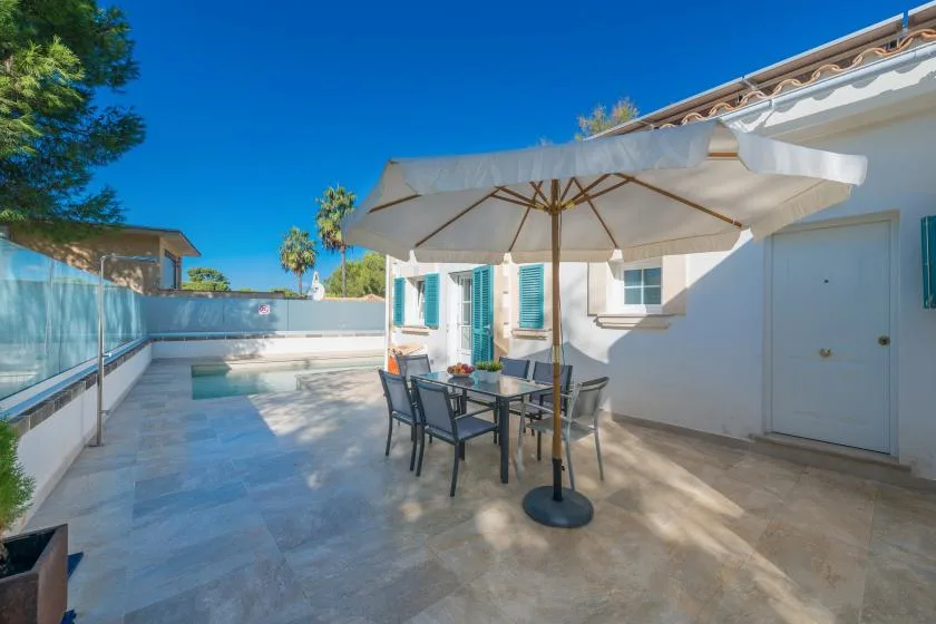Un patio exterior pavimentado tiene una mesa de comedor bajo una sombrilla grande.