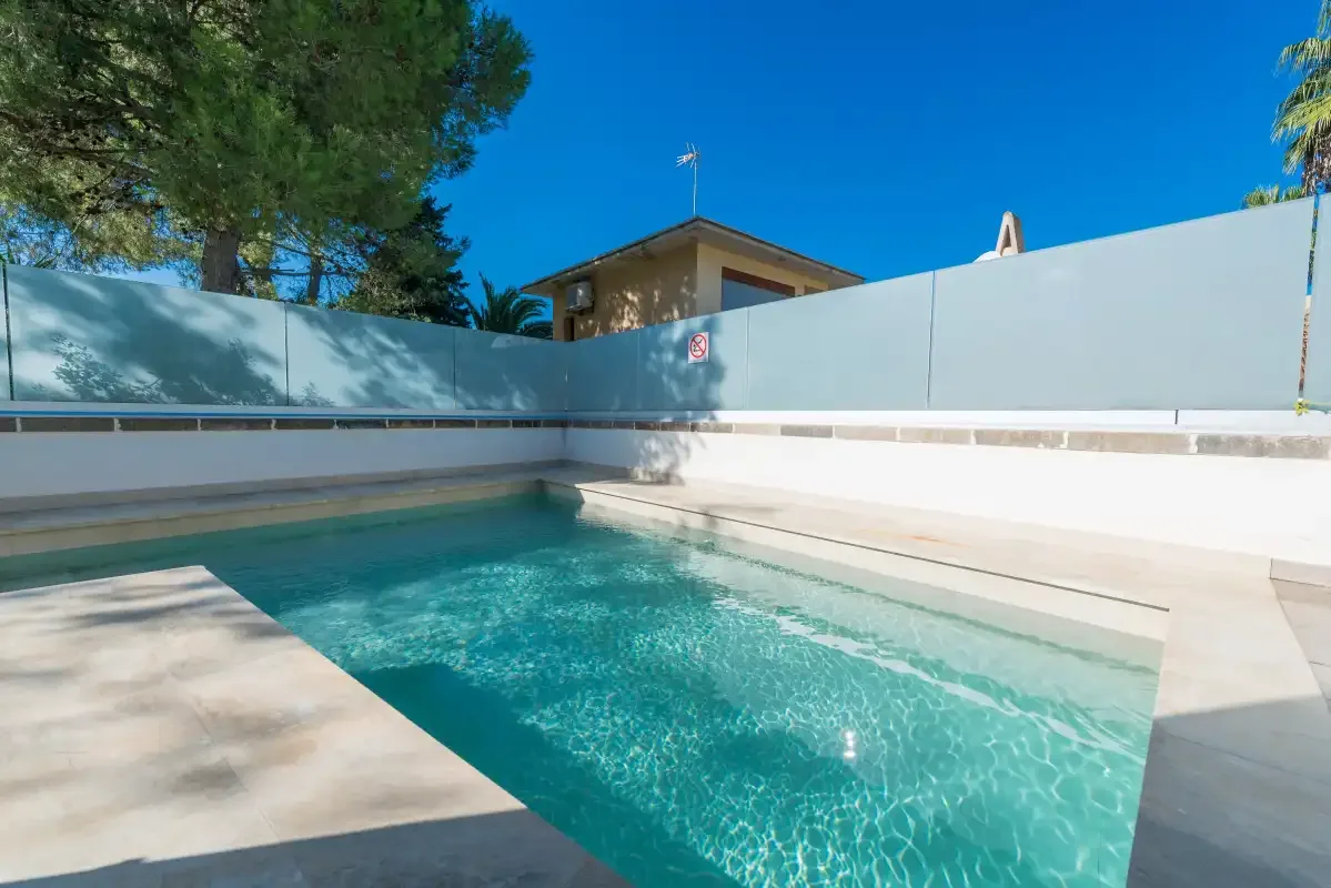 Una piscina al aire libre está rodeada por una terraza pavimentada clara y pantallas de privacidad.