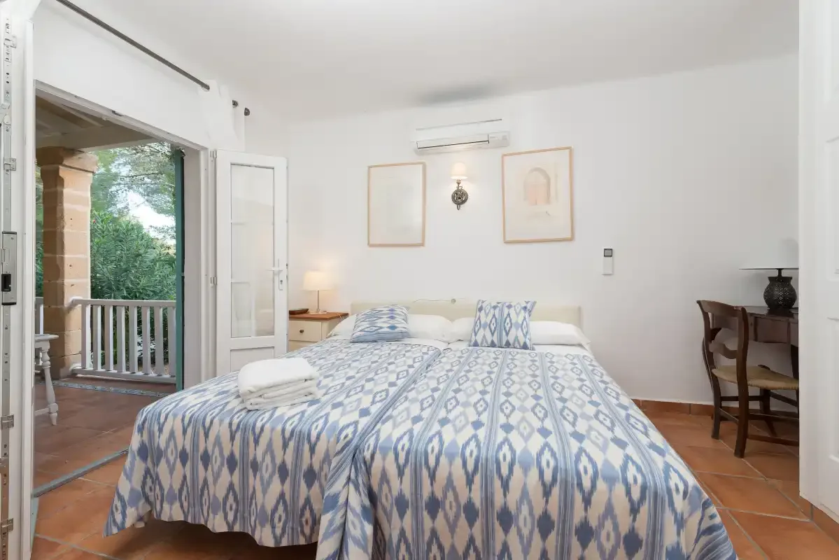 Un dormitorio luminoso con una colcha estampada y una puerta abierta al balcón.