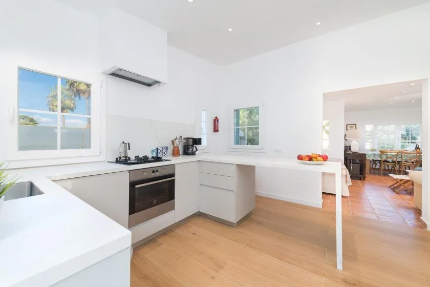 Una cocina luminosa con encimeras blancas y un comedor visible a través de la puerta.
