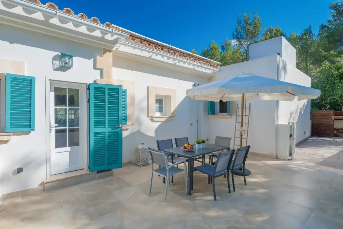 Un patio soleado con asientos al aire libre y una sombrilla grande junto a una casa blanca.
