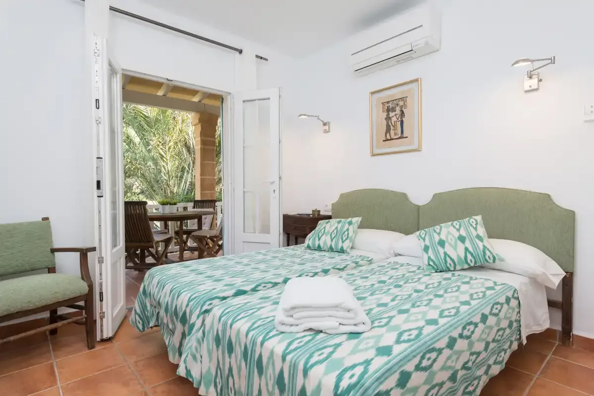 Dormitorio con una cama doble y una puerta abierta hacia un patio frondoso.