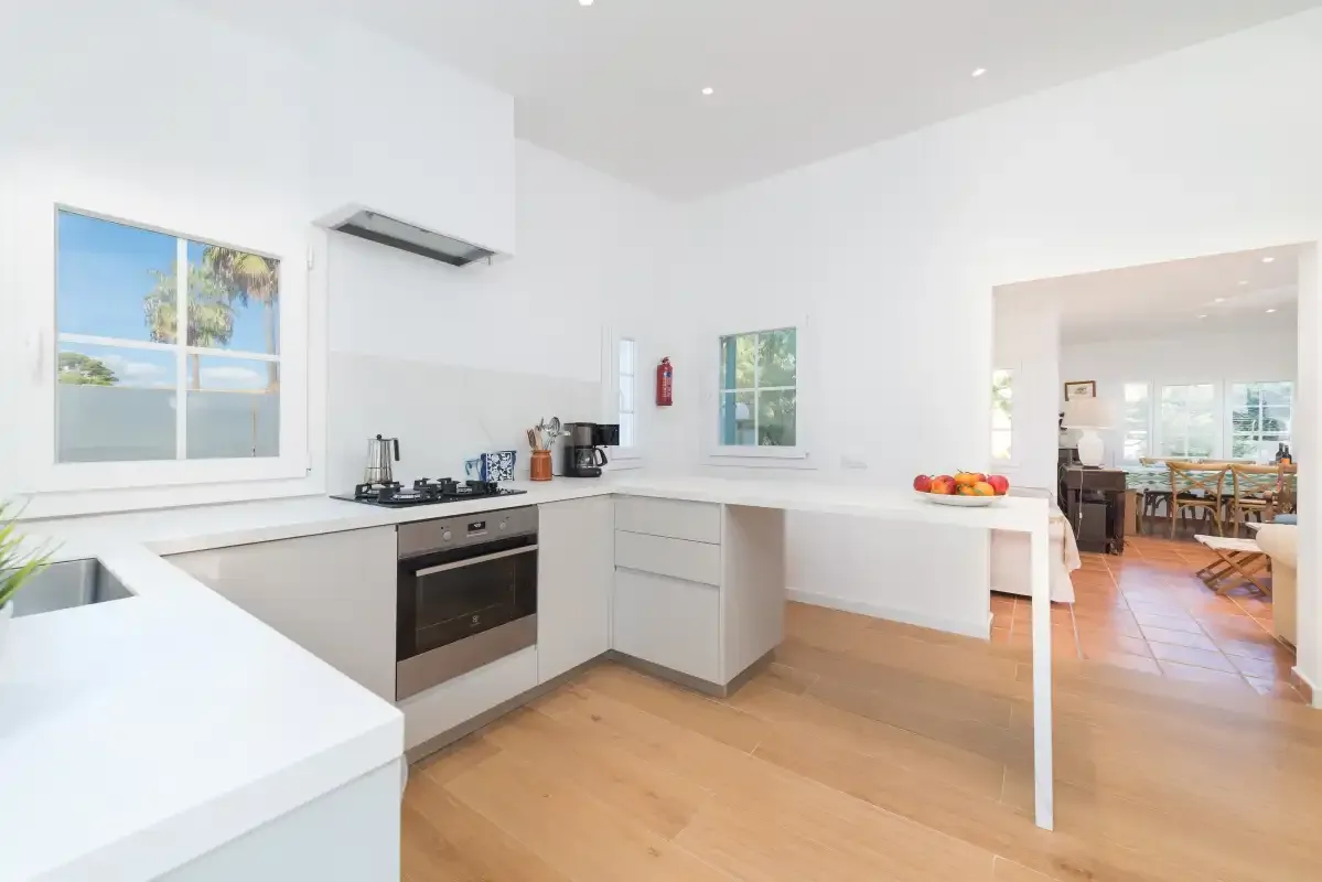 Una cocina luminosa con encimeras blancas y una abertura hacia el comedor.