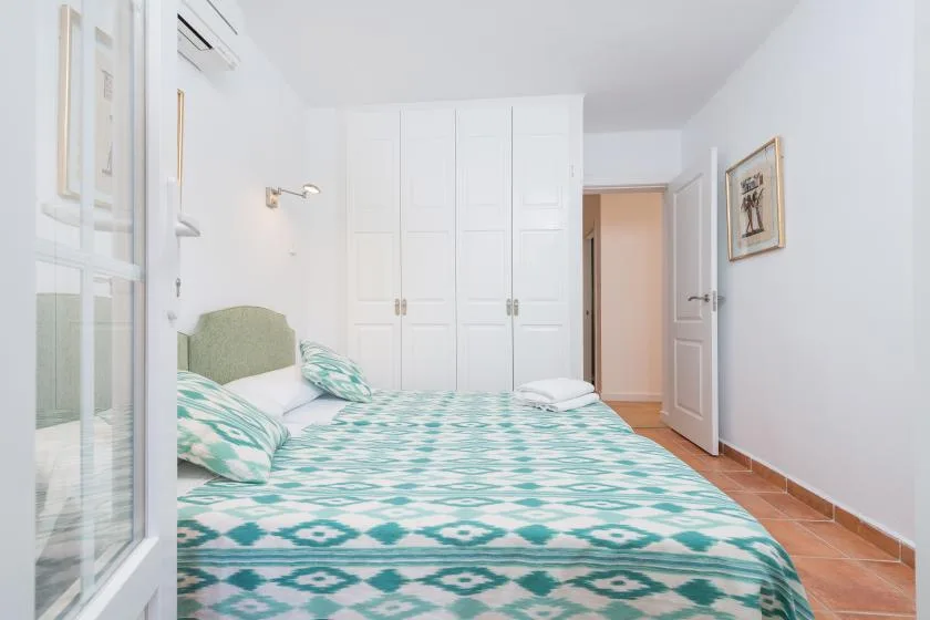 Un dormitorio luminoso con una cama cubierta de ropa de cama estampada en tonos turquesa y blanco.