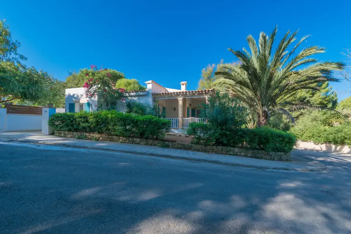 Una casa se encuentra detrás de un seto y palmeras junto a una carretera.
