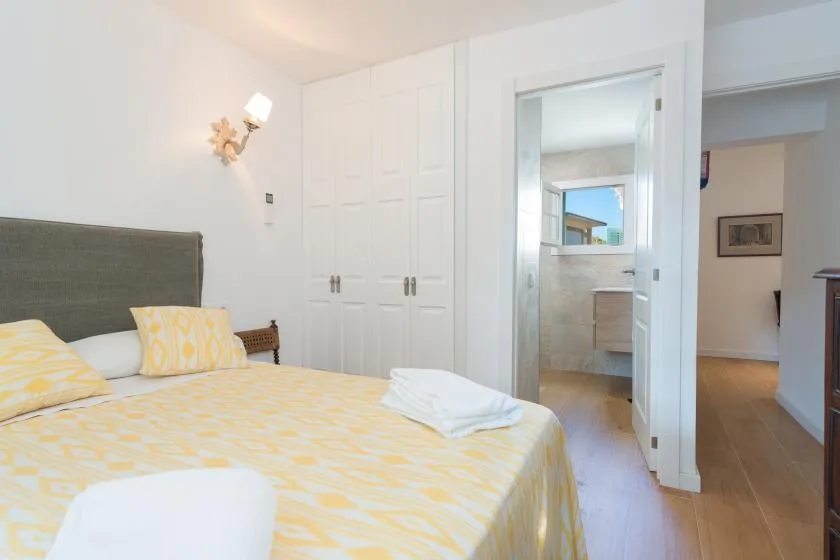 Un dormitorio con una colcha amarilla estampada y una puerta abierta al baño.