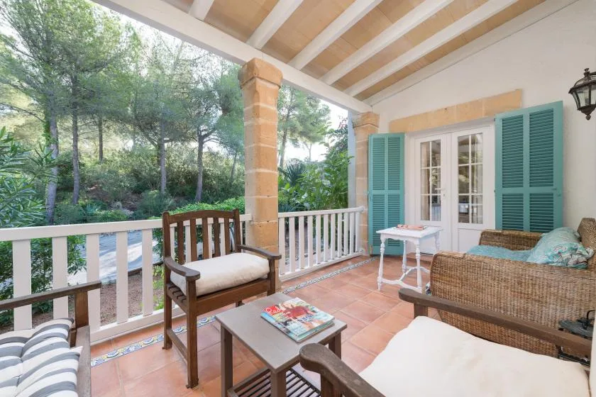 Un porche cubierto con asientos da a un patio arbolado y verde.