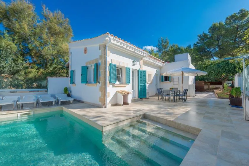 Una casa blanca da a un patio de baldosas junto a una piscina.