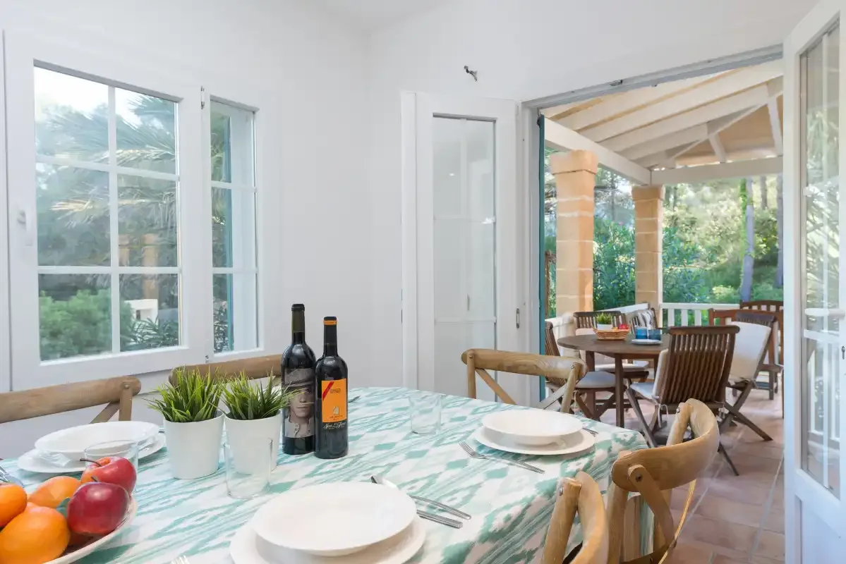 Comedor con la mesa puesta junto a puertas abiertas que dan a un patio cubierto.