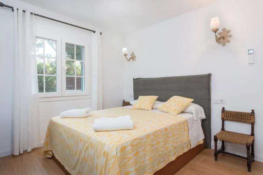 Un dormitorio con una cama doble vestida con ropa de cama amarilla clara junto a una ventana.