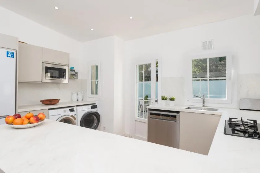 Una cocina blanca y luminosa con una isla grande y electrodomésticos de acero inoxidable.