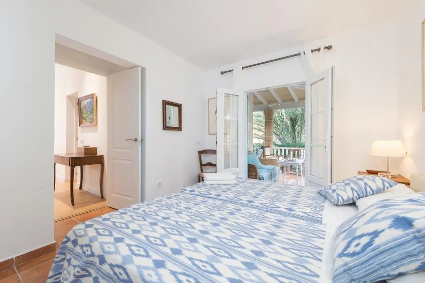 Un dormitorio luminoso con una colcha estampada y puertas abiertas que dan a un balcón.