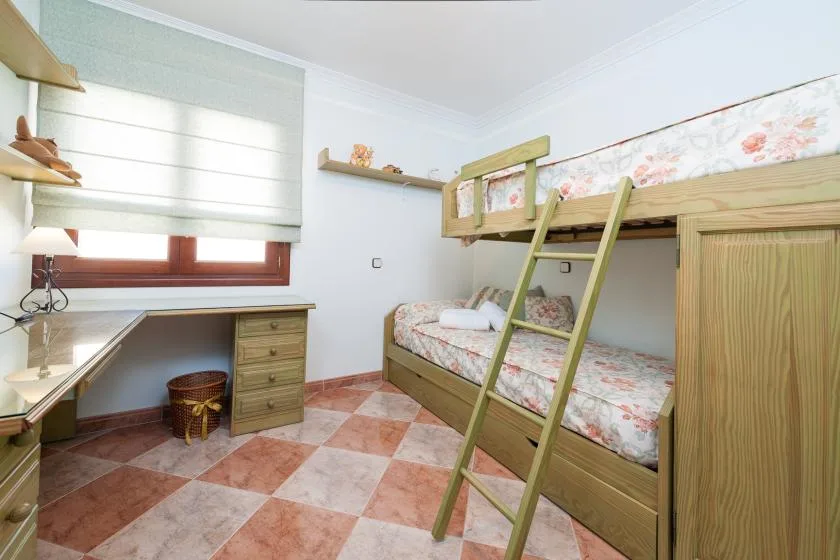 A bright bedroom with bunk beds, floral bedding, and a desk beneath the window.