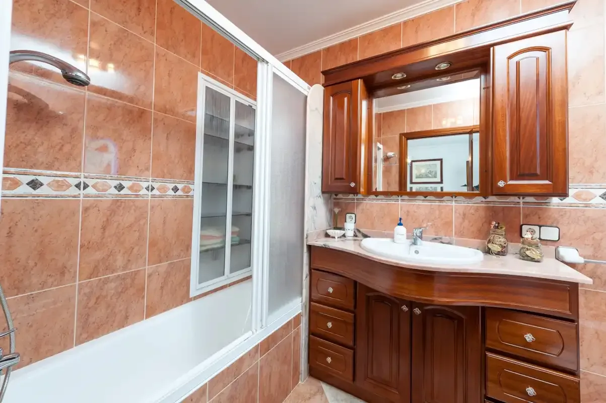 A bathroom with a bathtub and a wooden vanity beneath a mirror.