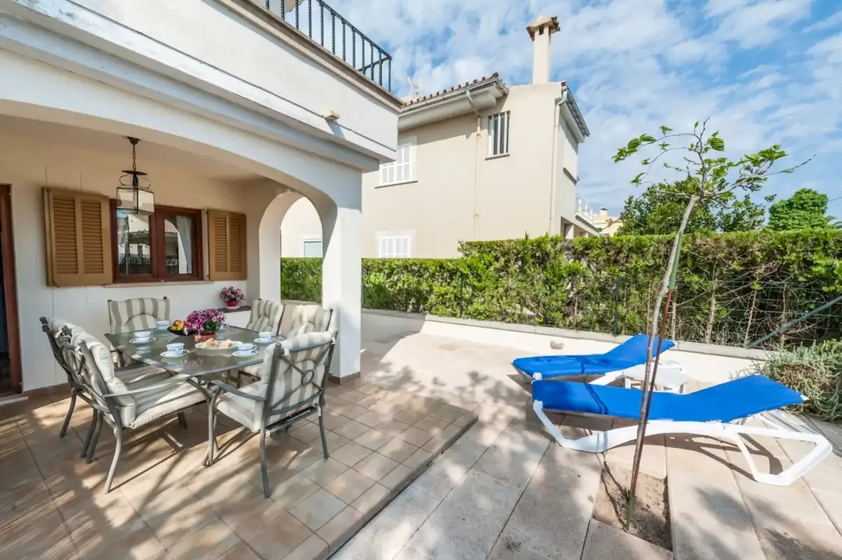 A tiled patio with outdoor seating and blue lounge chairs beside a garden.