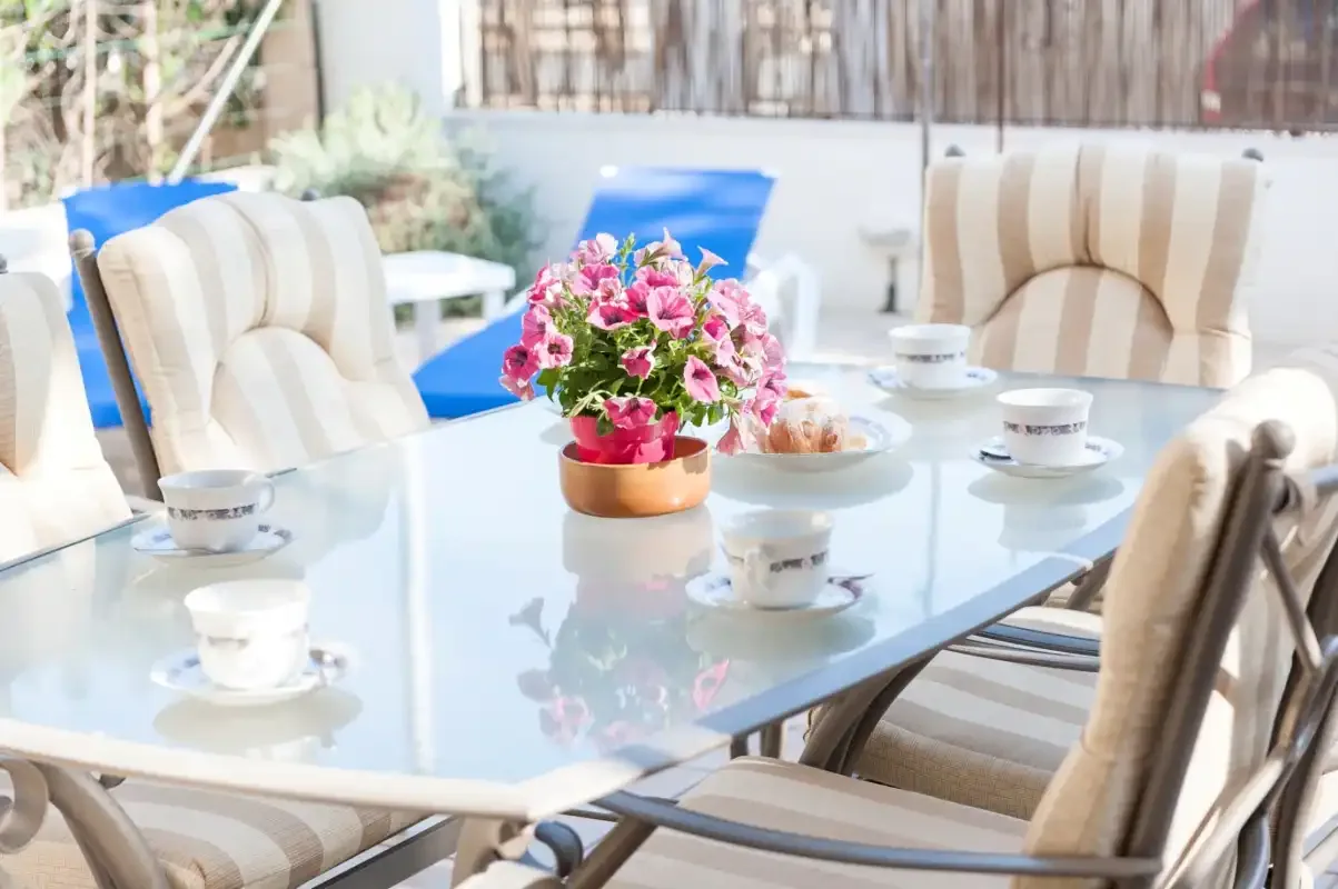 Outdoor dining area with a glass table set with cups and flowers.
