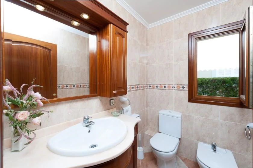 A tiled bathroom with a sink, toilet, and window.