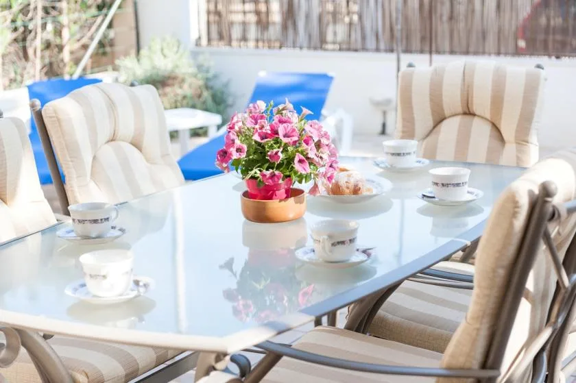 An outdoor dining table is set with cups and a flower arrangement.
